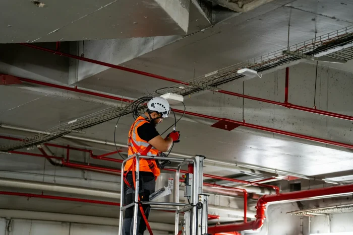 An engineer on a lift platform working on the services in a building ceiling