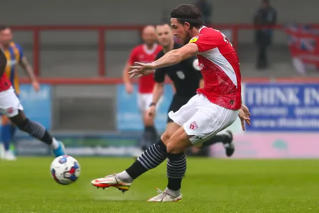 A footballer in red striking the ball from a penalty
